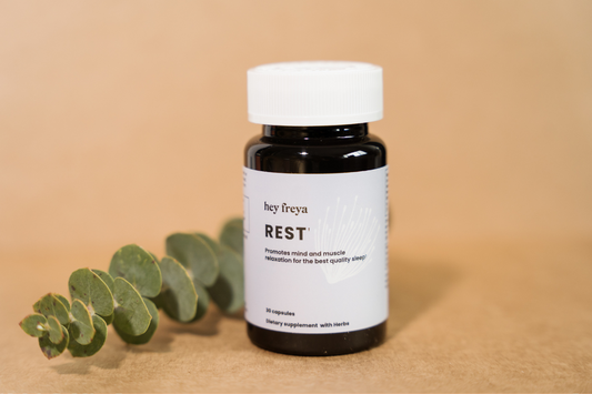A bottle of Hey Freya’s REST supplement with natural ingredients on a green background
