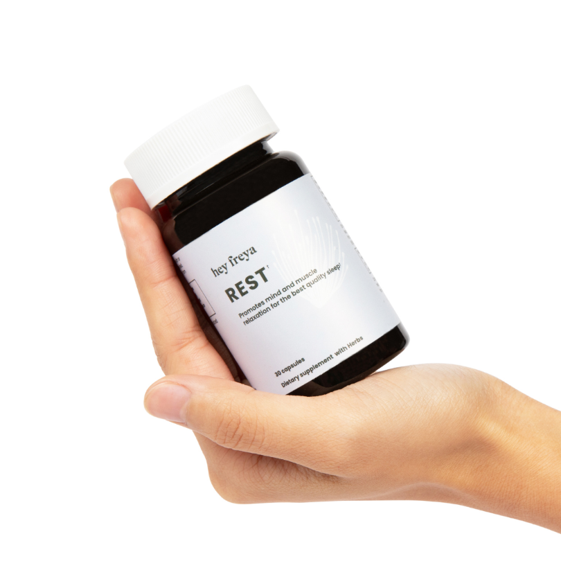 REST: Unique women's multivitamin and multimineral supplement promoting muscle and mind relaxation. An amber-colored bottle with a pale blue label resting in a woman’s hand inducing a sense of tranquility and wellness.