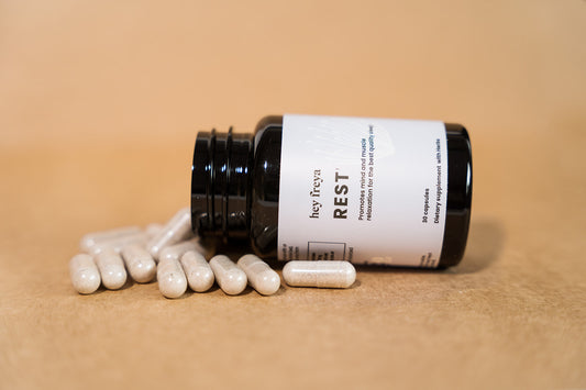 REST Multivitamin and Multimineral Supplement in Amber-Colored Bottle Laying Sideways Amongst Capsules, Promoting Restful Sleep.