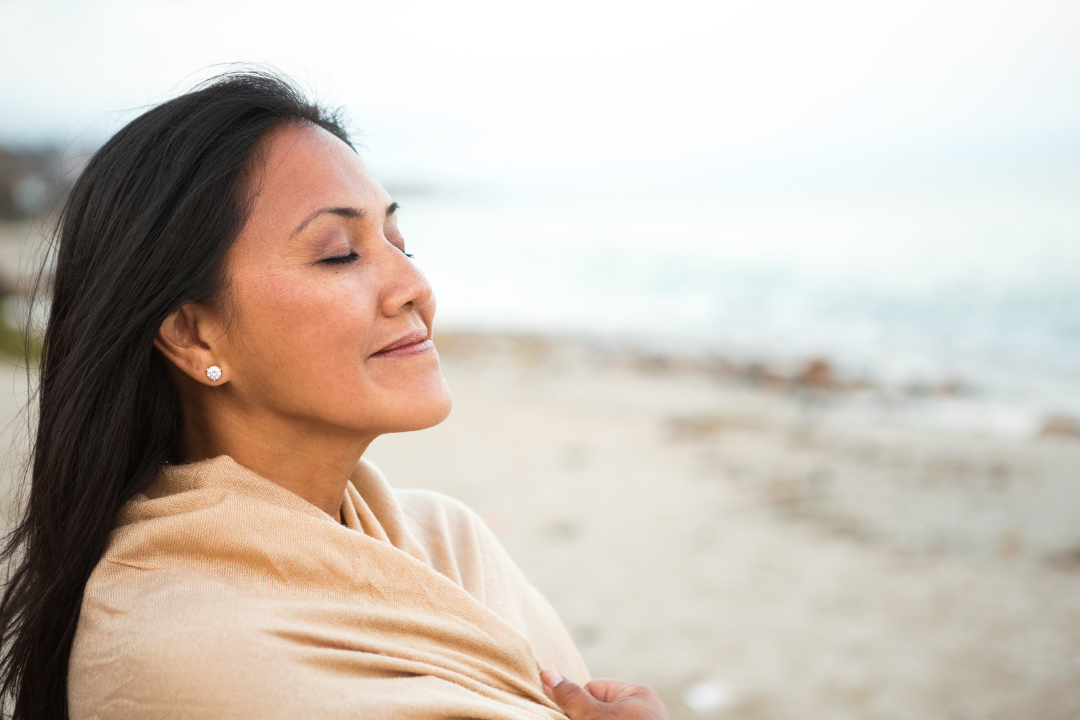 Serene Woman with Closed Eyes, Wrapped in a Shawl, Smiling on a Beach.