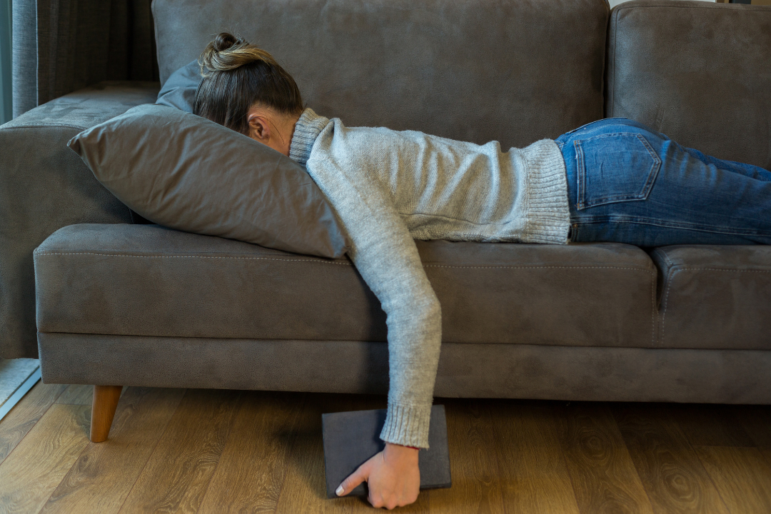 Fatigued Woman Lying Face Down on a Grey Couch.
