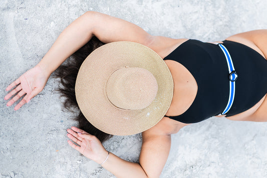 Midlife woman with adrenal fatigue lying on a beach in a black bathing suit with a hat over her face