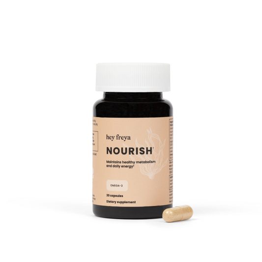 A stress reducing multi-vitamin and multi-mineral supplement for women called NOURISH, featuring an amber bottle in a few grey river rocks with a peach label that has 14 vitamins and minerals listed on it