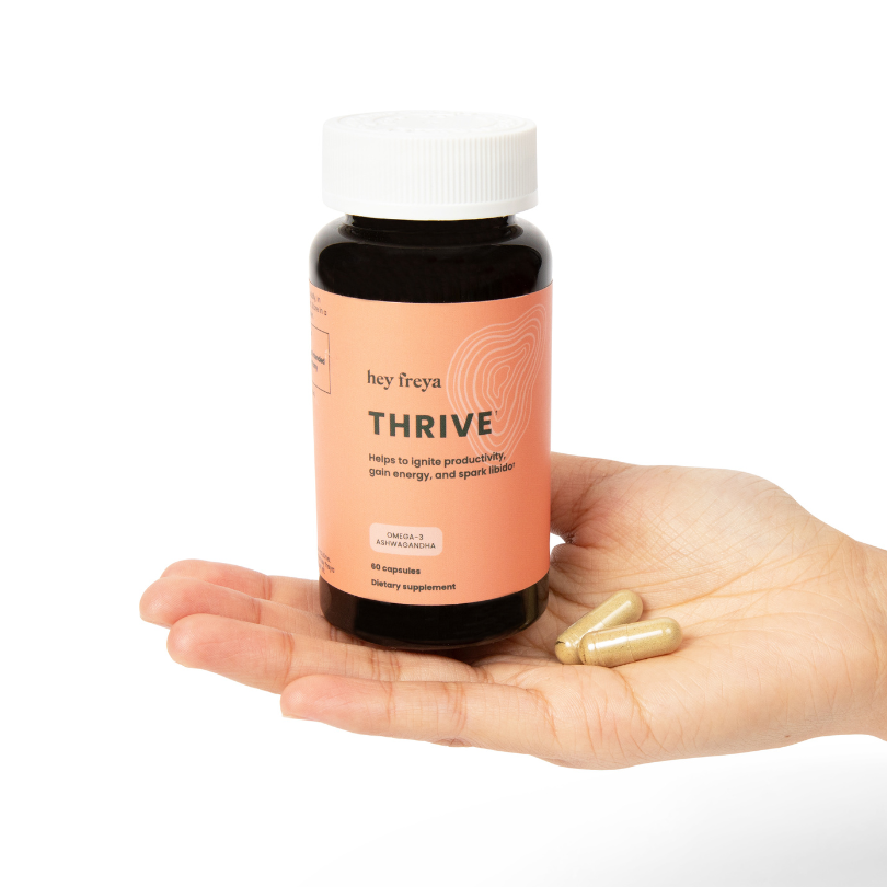 THRIVE - The Ultimate Stress Reliever and Best Female Libido Supplement: Each of the 60 Vegan Capsules Contains a Proprietary Blend of Green Tea, Rhodiola Root Extract, Eleuthero Root Extract, Phosphatidylserine, and Lavender Flower Extract for Enhanced Wellness. Presented in an Amber-Colored Bottle with a Dark Salmon Label resting on a woman's hand with a daily dose of hey freya's THRIVE capsules
